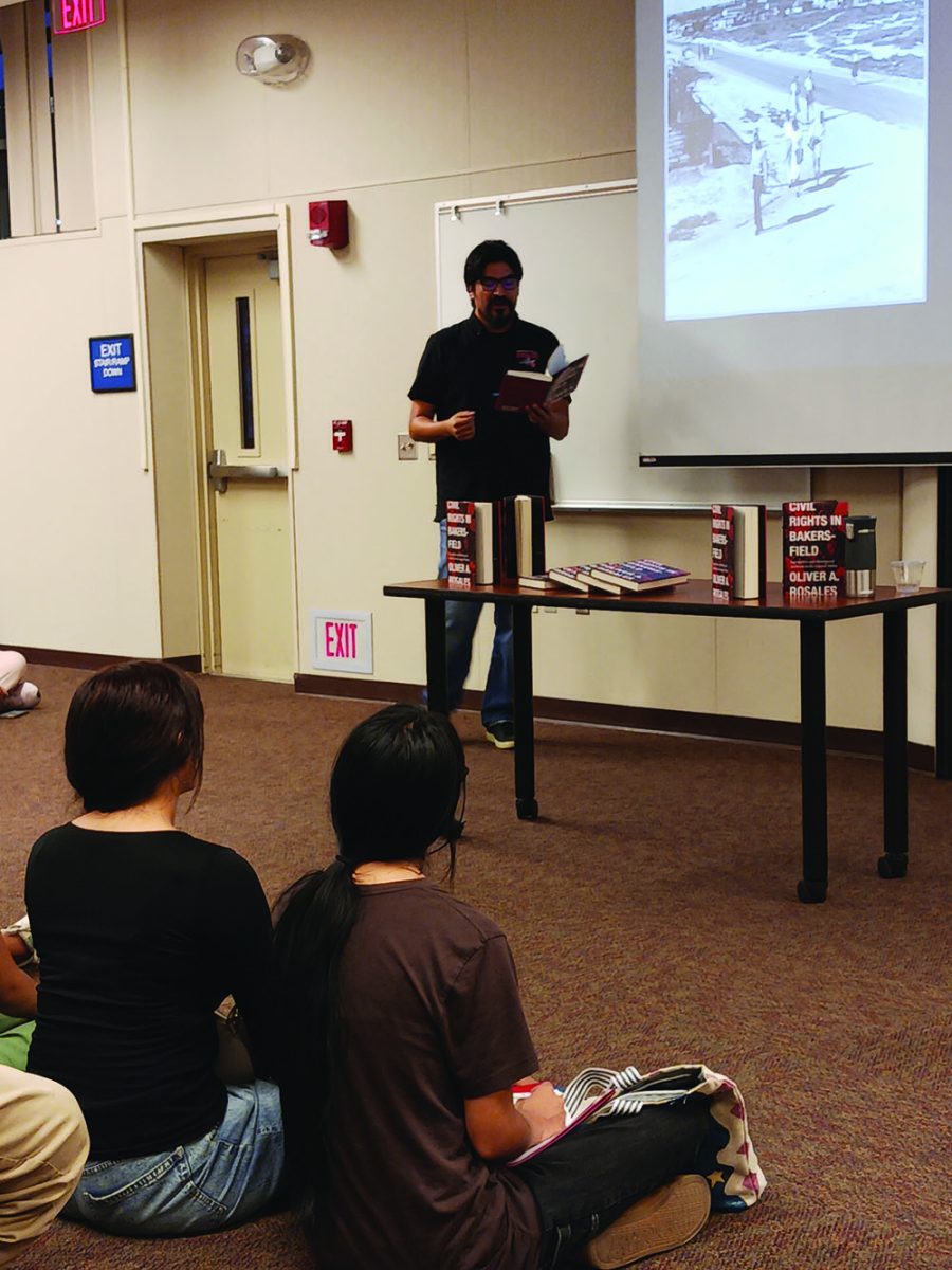 Man stands in front of sitting crowd reading his novel.